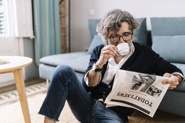 Älterer Mann trinkt Kaffee und liest Zeitung, während er zu Hause sitzt - JCZF00571