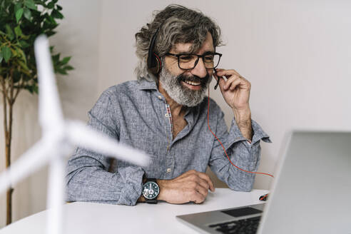 Smiling senior businessman with headset during video call on laptop at office - JCZF00599