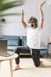 Älterer Mann, der Yoga übt, während er sich zu Hause am Laptop ein Tutorial ansieht - JCZF00620