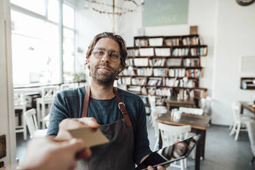 Customer's hand paying with credit card to male owner at cafe - JOSEF03898