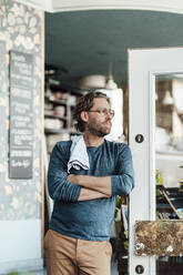 Male owner with arms crossed leaning at door in coffee shop - JOSEF03909