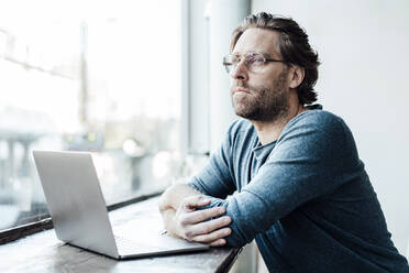 Nachdenklicher Mann mit Laptop auf dem Tisch in einem Cafe - JOSEF03932