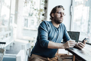 Mann mit Kaffeetasse am Laptop in einem Café sitzend - JOSEF03938