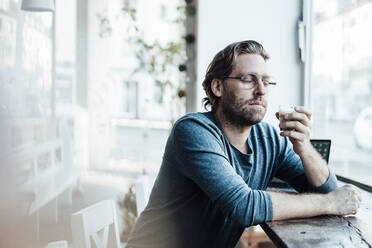 Mature man with eyes closed holding coffee cup at cafe - JOSEF03940