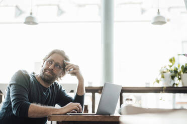 Thoughtful man with laptop looking away in coffee shop - JOSEF03945