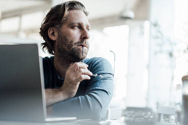 Man looking away while contemplating by laptop at cafe - JOSEF03946