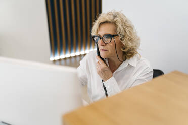 Receptionist looking at computer while talking on telephone in clinic - EGAF02136