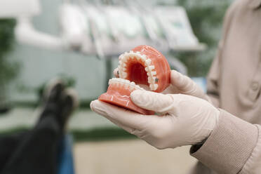 Arzt mit Schutzhandschuh hält Zahnersatz in der Klinik - EGAF02164