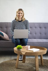 Blond mid adult woman sitting with laptop on sofa - GIOF11982