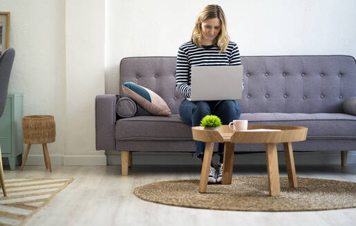 Frau benutzt Laptop, während sie zu Hause auf dem Sofa sitzt - GIOF11983