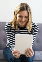 Mid adult woman smiling while using digital tablet at home - GIOF11987