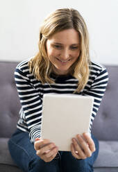 Mittlere erwachsene Frau lächelt, während sie ein digitales Tablet zu Hause benutzt - GIOF11987