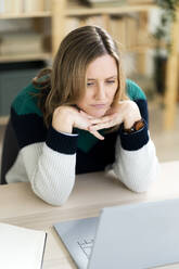 Frau mit Hand am Kinn schaut auf Laptop - GIOF12004