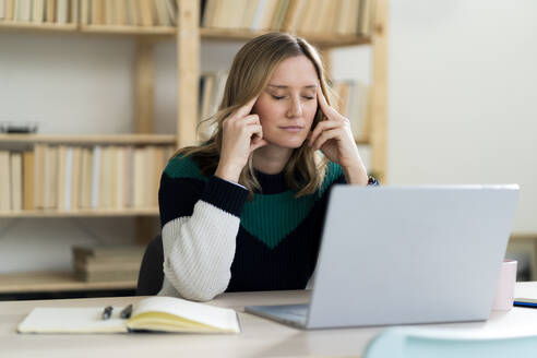 Mittlere erwachsene Frau sitzt mit dem Kopf in den Händen vor einem Laptop zu Hause - GIOF12007
