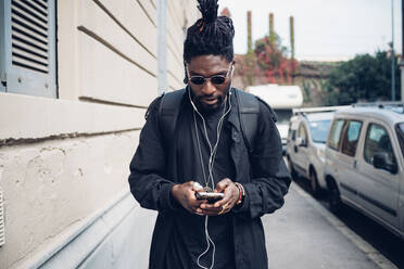 Young man with in-ear headphones using mobile phone on footpath - MEUF02309