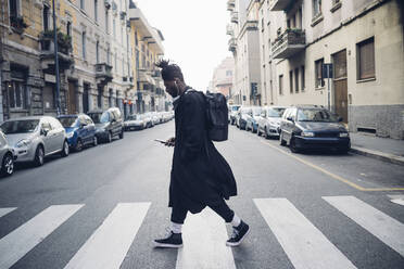 Fashionable man using mobile phone while crossing road in city - MEUF02311