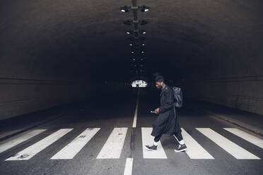 Young man with backpack walking on zebra crossing at underpass - MEUF02313