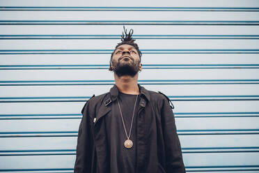 Young man looking up while standing in front of blue corrugated wall - MEUF02339