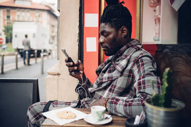 Modischer junger Mann mit Mobiltelefon in einem Straßencafé - MEUF02340