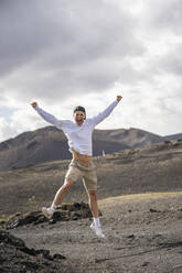 Aufgeregter männlicher Tourist mit ausgestreckten Armen beim Sprung auf den Vulkan el cuervo - SNF01182