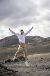 Excited male tourist with arms outstretched jumping on el cuervo volcano - SNF01182