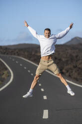 Young male tourist with arms outstretched jumping on road - SNF01195