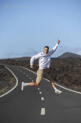 Smiling male tourist gesturing and jumping over road - SNF01196