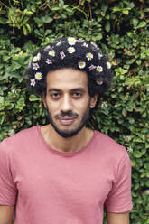 Afro young man with flowers in hair standing in front of plants - IFRF00486