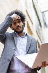 Worried male professional holding laptop looking away - IFRF00492