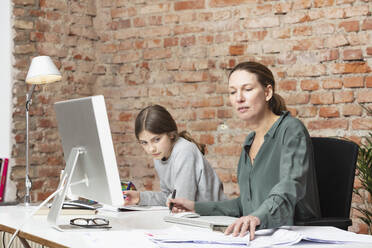 Berufstätige Frau arbeitet neben ihrer Tochter, die am Schreibtisch lernt - DHEF00609