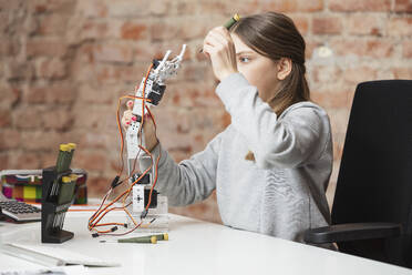 Mädchen hält Roboterarm und Arbeitswerkzeug am Tisch - DHEF00618