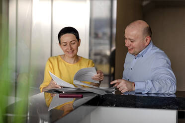 Smiling businesswoman reading document while discussing with male colleague in modern office - OGF00991