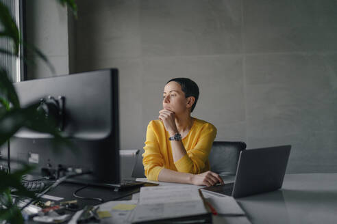 Thoughtful businesswoman looking away while sitting at desk in office - OGF01005