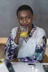 Female entrepreneur drinking juice while sitting in cafeteria - PNAF01245