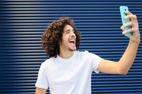 Cheerful young man making face while taking selfie through mobile phone - AODF00370