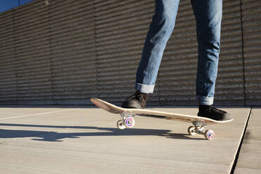 Junger Mann fährt Skateboard auf Hartholzboden an einem sonnigen Tag - AODF00385