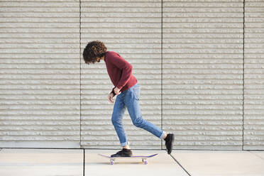 Lockenhaariger Mann fährt mit dem Skateboard an der Wand - AODF00386