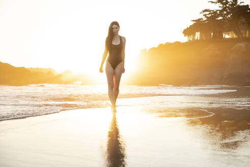 Fashion model in black one piece swimsuit walking in water during sunset - ISPF00067
