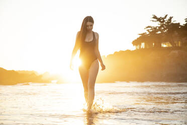 Weibliches Modell in schwarzem Badeanzug geht bei Sonnenuntergang am Strand spazieren - ISPF00068