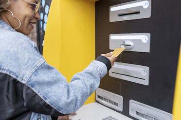 Lächelnde Frau beim Einführen einer Kreditkarte in einen Geldautomaten - RFTF00024