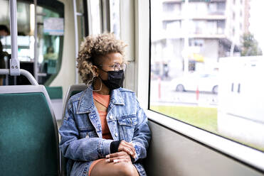 Mittlere erwachsene Frau mit Maske schaut durch ein Straßenbahnfenster - RFTF00027