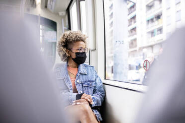 Frau mit Gesichtsschutzmaske schaut durch ein Straßenbahnfenster - RFTF00028