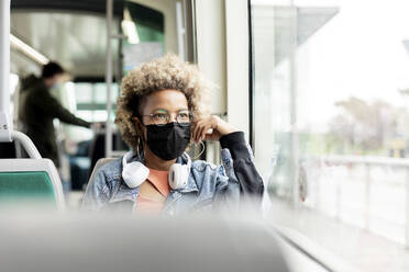Woman wearing mask looking through window while traveling in tram - RFTF00031