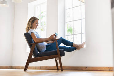 Mid adult woman using digital tablet while sitting on armchair at home - SBOF03377