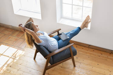 Woman with digital tablet relaxing on chair in front of window at home - SBOF03379