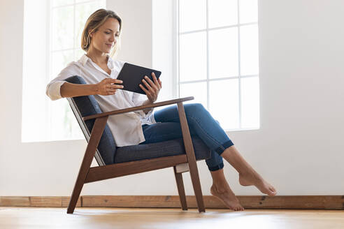 Frau sitzt auf einem Sessel und schaut auf ein digitales Tablet - SBOF03390