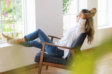 Relaxed woman with arms raised sitting on chair at home - SBOF03396