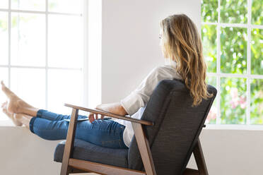 Frau mit hochgelegten Füßen sitzt auf einem Stuhl zu Hause - SBOF03399