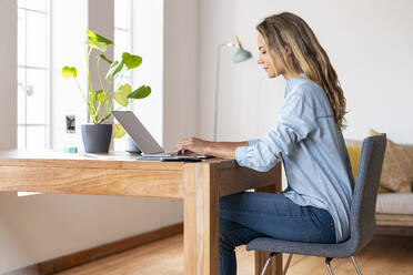 Concentrated businesswoman working on laptop at home office - SBOF03404