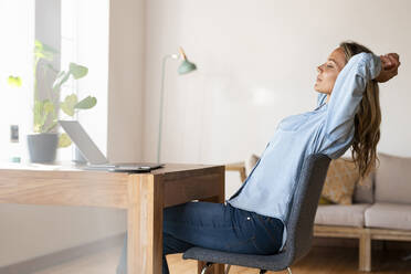 Relaxed female entrepreneur with eyes closed sitting in front of laptop at home - SBOF03405